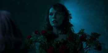 Movie still from “Paradise Hills” (2019), directed by Alice Waddington – A woman with long curly hair wearing a dress and holding a bouquet of red roses; Close Up shot, Over the shoulder angle