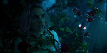 Movie still from “Paradise Hills” (2019), directed by Alice Waddington – A woman in a white sweater standing next to a bush; Close Up shot, Over the shoulder angle