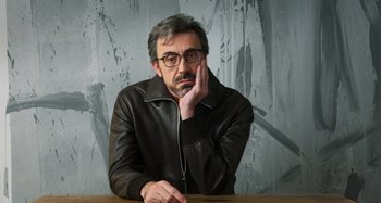 Movie still from “Parallel Mothers” (2021), directed by Pedro Almodóvar – A man in a leather jacket sitting at a wooden table; Close Up shot, Low angle