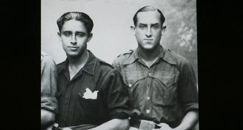 Movie still from “Parallel Mothers” (2021), directed by Pedro Almodóvar – A couple of men standing next to each other in a black and white photo; Close Up shot, Low angle