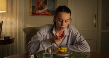 Movie still from “Parallel Mothers” (2021), directed by Pedro Almodóvar – A woman sitting at a table with a bowl of fruit in front of her; Medium shot, Over the shoulder angle