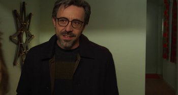 Movie still from “Parallel Mothers” (2021), directed by Pedro Almodóvar – A person wearing glasses and a jacket; Close Up shot, Over the shoulder angle