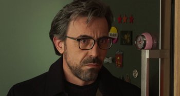 Movie still from “Parallel Mothers” (2021), directed by Pedro Almodóvar – A person wearing glasses and a black shirt; Close Up shot, Over the shoulder angle
