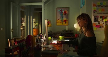 Movie still from “Parallel Mothers” (2021), directed by Pedro Almodóvar – A woman sitting in front of a computer in a room; Medium shot, High angle