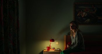 Movie still from “Parallel Mothers” (2021), directed by Pedro Almodóvar – A woman sitting on a chair in front of a lamp; Medium shot, High angle