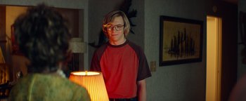 Movie still from “My Friend Dahmer” (2017), directed by Marc Meyers – A man standing in front of a lamp in a living room; Medium shot, Over the shoulder angle