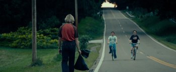 Movie still from “My Friend Dahmer” (2017), directed by Marc Meyers – A man holding a bag and a woman riding a bike down a street; Wide shot, Over the shoulder angle