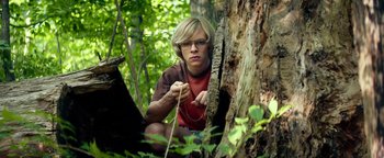 Movie still from “My Friend Dahmer” (2017), directed by Marc Meyers – A man in a red shirt is tying a rope around a tree; Medium shot, Low angle