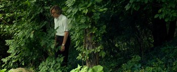 Movie still from “My Friend Dahmer” (2017), directed by Marc Meyers – A man standing next to a tree in the woods; Medium shot, Low angle