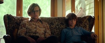 Movie still from “My Friend Dahmer” (2017), directed by Marc Meyers – Two people sitting on a couch in front of a window; Medium shot, Low angle
