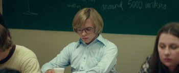 Movie still from “My Friend Dahmer” (2017), directed by Marc Meyers – A man sitting in front of a chalkboard holding a drink; Medium shot, Over the shoulder angle