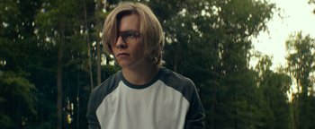 Movie still from “My Friend Dahmer” (2017), directed by Marc Meyers – A man with blonde hair wearing glasses and a white and black t - shirt; Close Up shot, Over the shoulder angle
