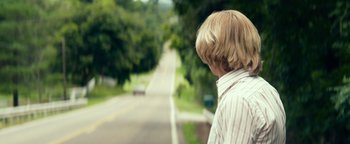 Movie still from “My Friend Dahmer” (2017), directed by Marc Meyers – A young boy standing on the side of a road; Close Up shot, Over the shoulder angle