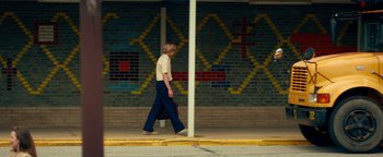 Movie still from “My Friend Dahmer” (2017), directed by Marc Meyers – A man walking down the street with a skateboard; Wide shot, Low angle
