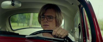 Movie still from “My Friend Dahmer” (2017), directed by Marc Meyers – A man driving a car wearing glasses and a white t - shirt; Close Up shot, Low angle