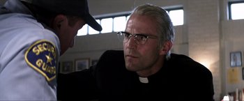 Movie still from “Parker” (2013), directed by Taylor Hackford – A man in glasses and a priest's outfit is talking to another man in glasses; Close Up shot, Over the shoulder angle