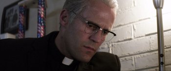Movie still from “Parker” (2013), directed by Taylor Hackford – A man wearing glasses and a priest's outfit; Close Up shot, Low angle