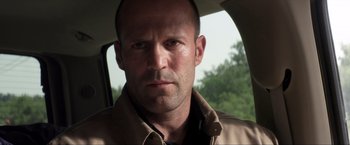 Movie still from “Parker” (2013), directed by Taylor Hackford – A person in a car with trees in the background; Close Up shot, Over the shoulder angle