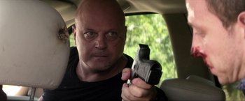 Movie still from “Parker” (2013), directed by Taylor Hackford – A man holding a gun in the back seat of a car; Close Up shot, Low angle