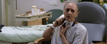 Movie still from “Parker” (2013), directed by Taylor Hackford – An older man in a hospital gown talking on a cell phone; Close Up shot, Over the shoulder angle