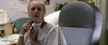 Movie still from “Parker” (2013), directed by Taylor Hackford – An older man in a hospital gown holding a neck tie; Close Up shot, Over the shoulder angle