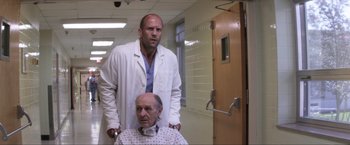 Movie still from “Parker” (2013), directed by Taylor Hackford – A man standing next to an older man in a hospital room; Medium shot, Low angle