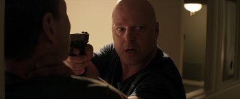Movie still from “Parker” (2013), directed by Taylor Hackford – A bald man holding a gun in a room; Close Up shot, Over the shoulder angle