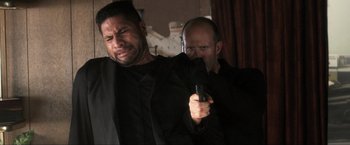 Movie still from “Parker” (2013), directed by Taylor Hackford – A man holding a gun while another man is crying; Close Up shot, Over the shoulder angle