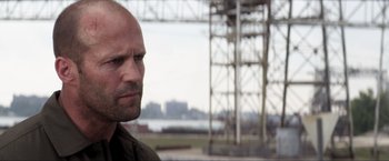 Movie still from “Parker” (2013), directed by Taylor Hackford – A man with a beard is standing in front of a power tower; Close Up shot, Over the shoulder angle