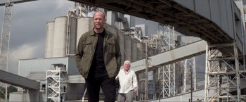 Movie still from “Parker” (2013), directed by Taylor Hackford – A man standing next to an older woman in front of an industrial building; Medium shot, Low angle