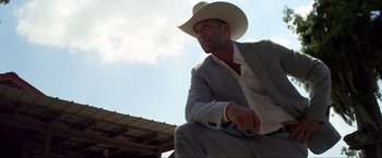 Movie still from “Parker” (2013), directed by Taylor Hackford – A man wearing a cowboy hat sitting on the ground; Medium shot, Low angle