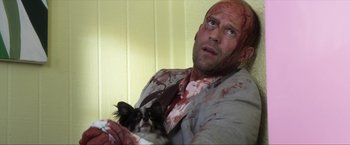 Movie still from “Parker” (2013), directed by Taylor Hackford – A man holding a dog with blood all over his face; Close Up shot, High angle