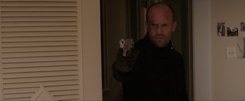 Movie still from “Parker” (2013), directed by Taylor Hackford – A bald man holding a gun in front of a mirror; Medium shot, Low angle