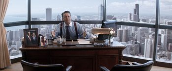 Movie still from “Parker” (2013), directed by Taylor Hackford – A man sitting at a desk in front of a large window; Medium shot, Over the shoulder angle