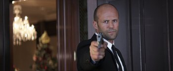 Movie still from “Parker” (2013), directed by Taylor Hackford – A man in a suit and tie holding a gun; Close Up shot, Low angle