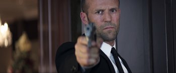 Movie still from “Parker” (2013), directed by Taylor Hackford – A man in a suit and tie holding a gun; Close Up shot, Low angle