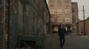 Movie still from “Paterson” (2016), directed by Jim Jarmusch – A man walking down a street near a brick building; Extreme Wide shot, Low angle