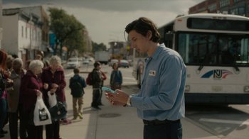 Movie still from “Paterson” (2016), directed by Jim Jarmusch – A man standing on a sidewalk looking at his cell phone; Medium shot, Low angle