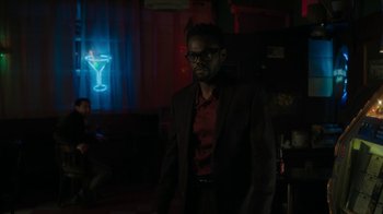 Movie still from “Paterson” (2016), directed by Jim Jarmusch – A man standing in a dark room with glasses on his face; Medium shot, Over the shoulder angle