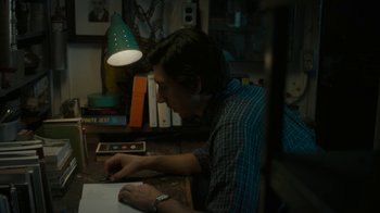 Movie still from “Paterson” (2016), directed by Jim Jarmusch – A man sitting at a table with a book in front of him; Medium shot, High angle