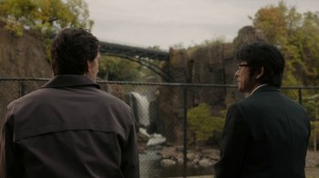 Movie still from “Paterson” (2016), directed by Jim Jarmusch – Two men standing next to each other in front of a waterfall; Medium shot, Over the shoulder angle