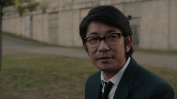 Movie still from “Paterson” (2016), directed by Jim Jarmusch – A man wearing a suit and tie standing in front of a building; Close Up shot, Over the shoulder angle