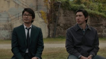 Movie still from “Paterson” (2016), directed by Jim Jarmusch – Two men in suits sitting in a grassy area; Medium shot, Over the shoulder angle