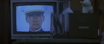 Movie still from “Patriot Games” (1992), directed by Phillip Noyce – A television screen with a picture of a man wearing a hat; Extreme Close Up shot, Over the shoulder angle