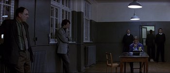 Movie still from “Patriot Games” (1992), directed by Phillip Noyce – A man leaning up against a wall next to a chair; Wide shot, Over the shoulder angle