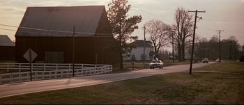 Movie still from “Patriot Games” (1992), directed by Phillip Noyce – A car driving down a road next to a barn; Extreme Wide shot, Low angle