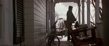 Movie still from “Patriot Games” (1992), directed by Phillip Noyce – A man on a porch with a bicycle and swing; Wide shot, Low angle