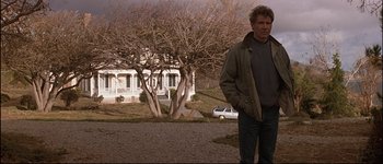 Movie still from “Patriot Games” (1992), directed by Phillip Noyce – A man standing in front of a house on a dirt road; Medium shot, Low angle