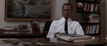 Movie still from “Patriot Games” (1992), directed by Phillip Noyce – A man sitting at a desk in front of a picture; Medium shot, Low angle