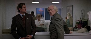 Movie still from “Patriot Games” (1992), directed by Phillip Noyce – A man in a suit standing next to another man in a suit; Medium shot, Over the shoulder angle
